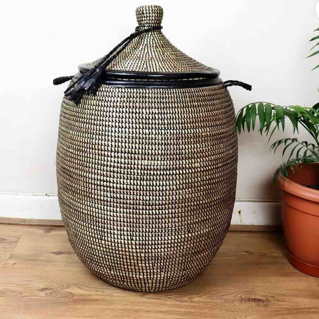 Woven basket with a lid on a wooden floor next to a plant