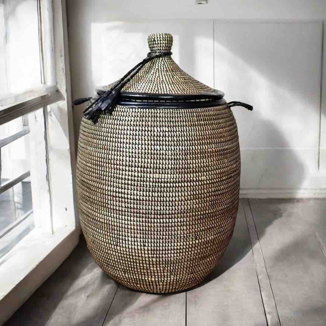 Woven storage basket with a lid on a wooden floor near a window.