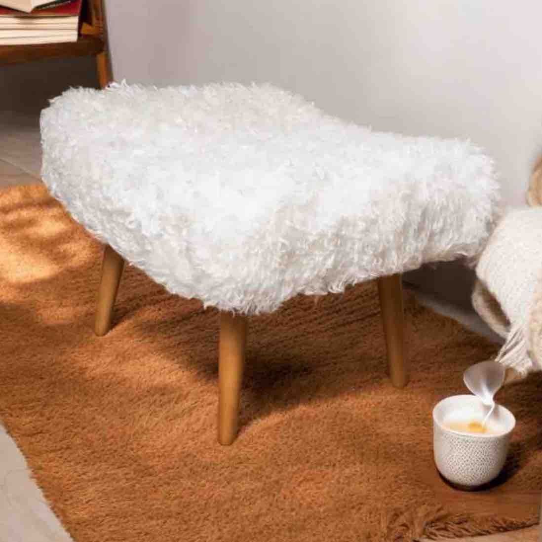 White fluffy ottoman on a brown rug with a cup and saucer in the foreground.
