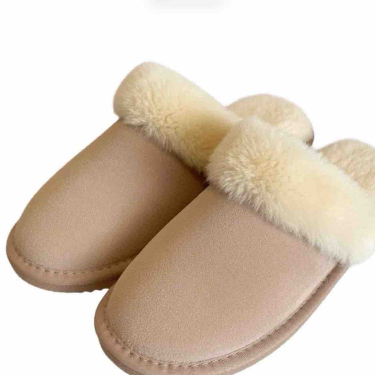 A pair of slip-on mule slippers with a beige suede-like upper and thick cream faux-fur trim around the opening, shown on a plain white background.