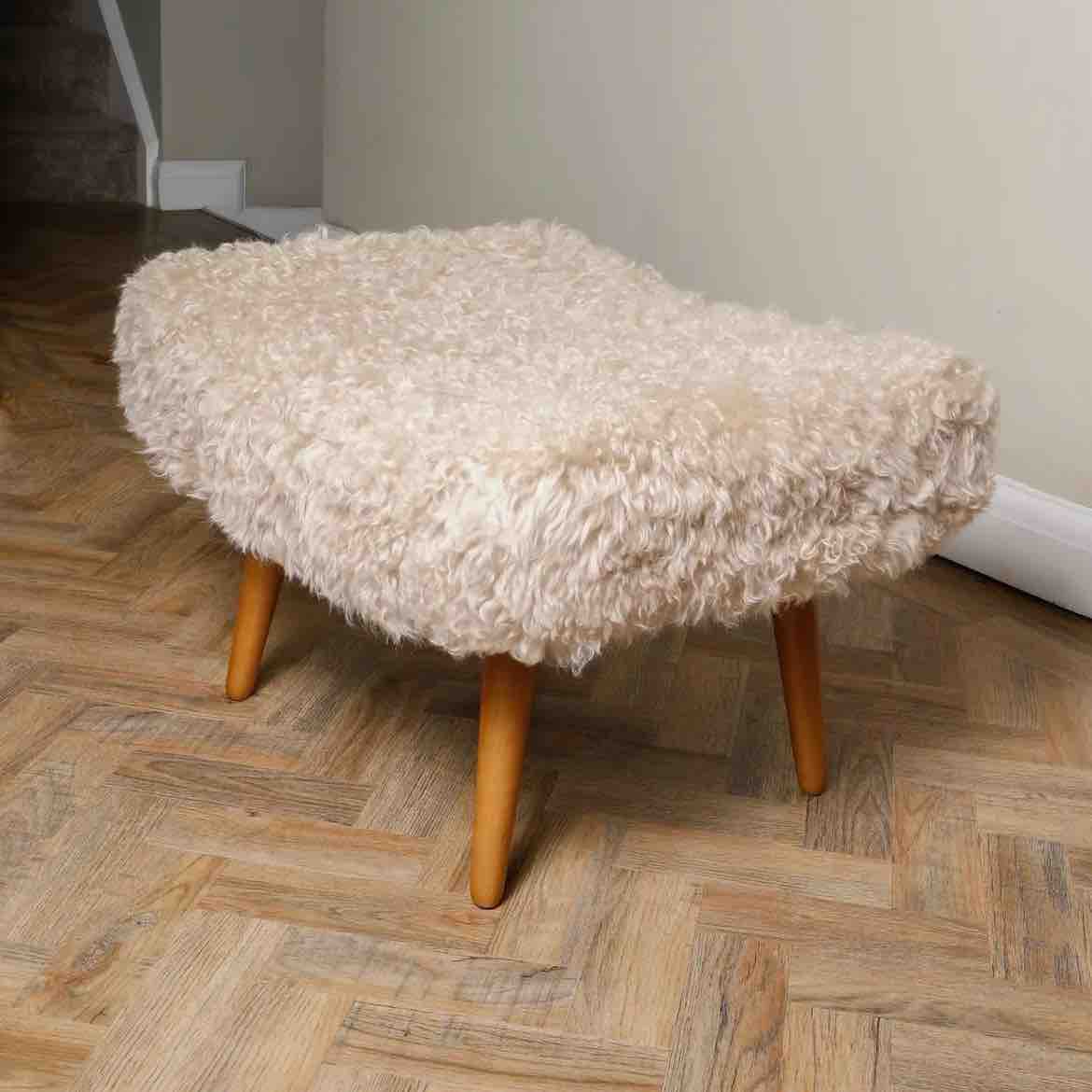 Fluffy ottoman with wooden legs on a herringbone wood floor.