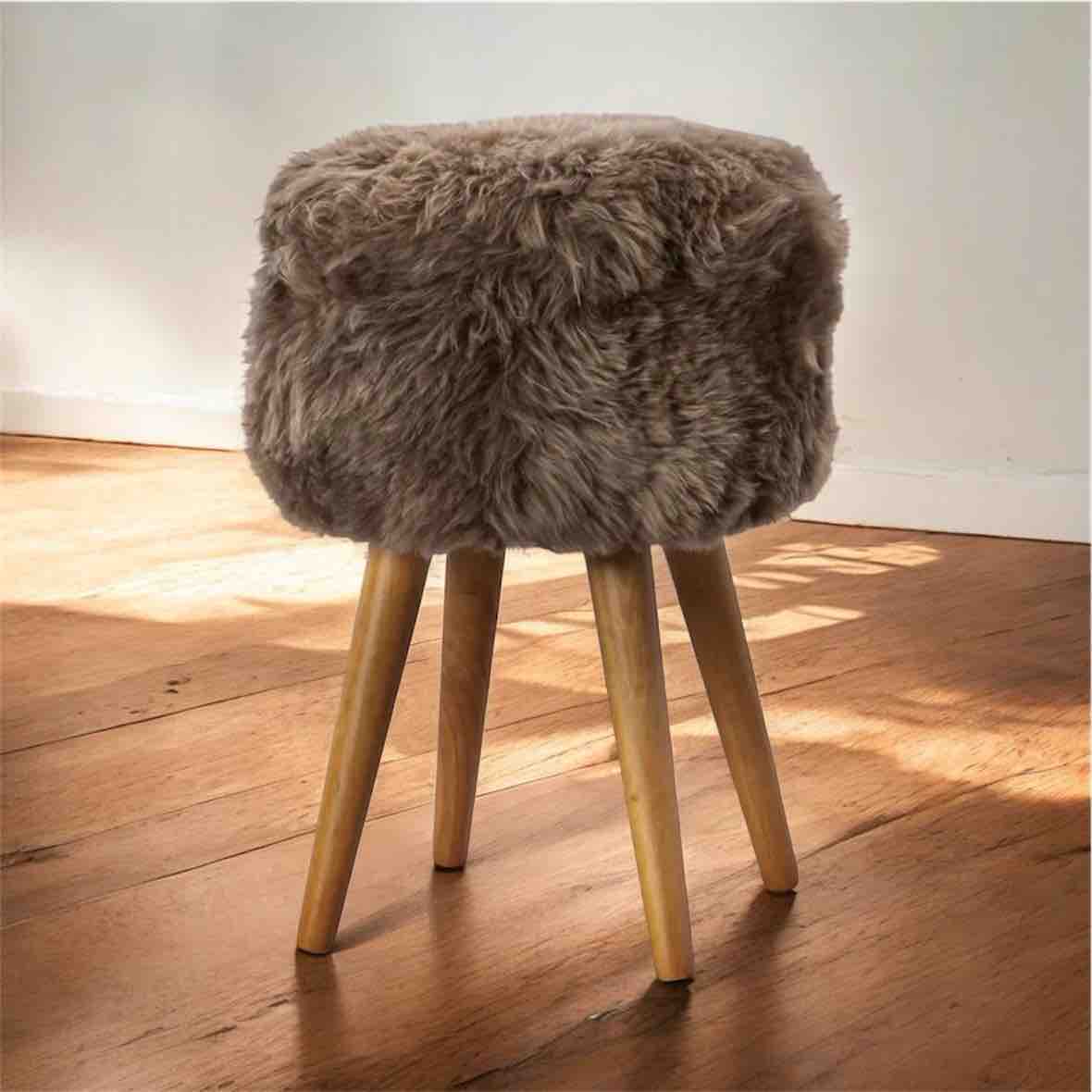 Stool with fur-covered top and wooden legs on a wooden floor.