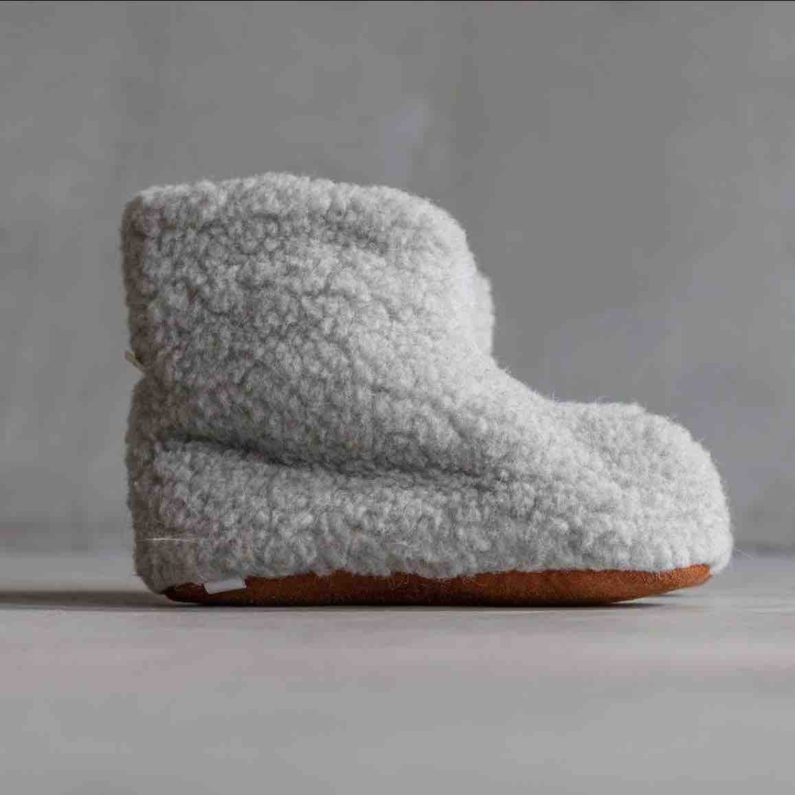A single plush shearling slipper boot in light gray with a brown sole, photographed against a neutral gray background.
