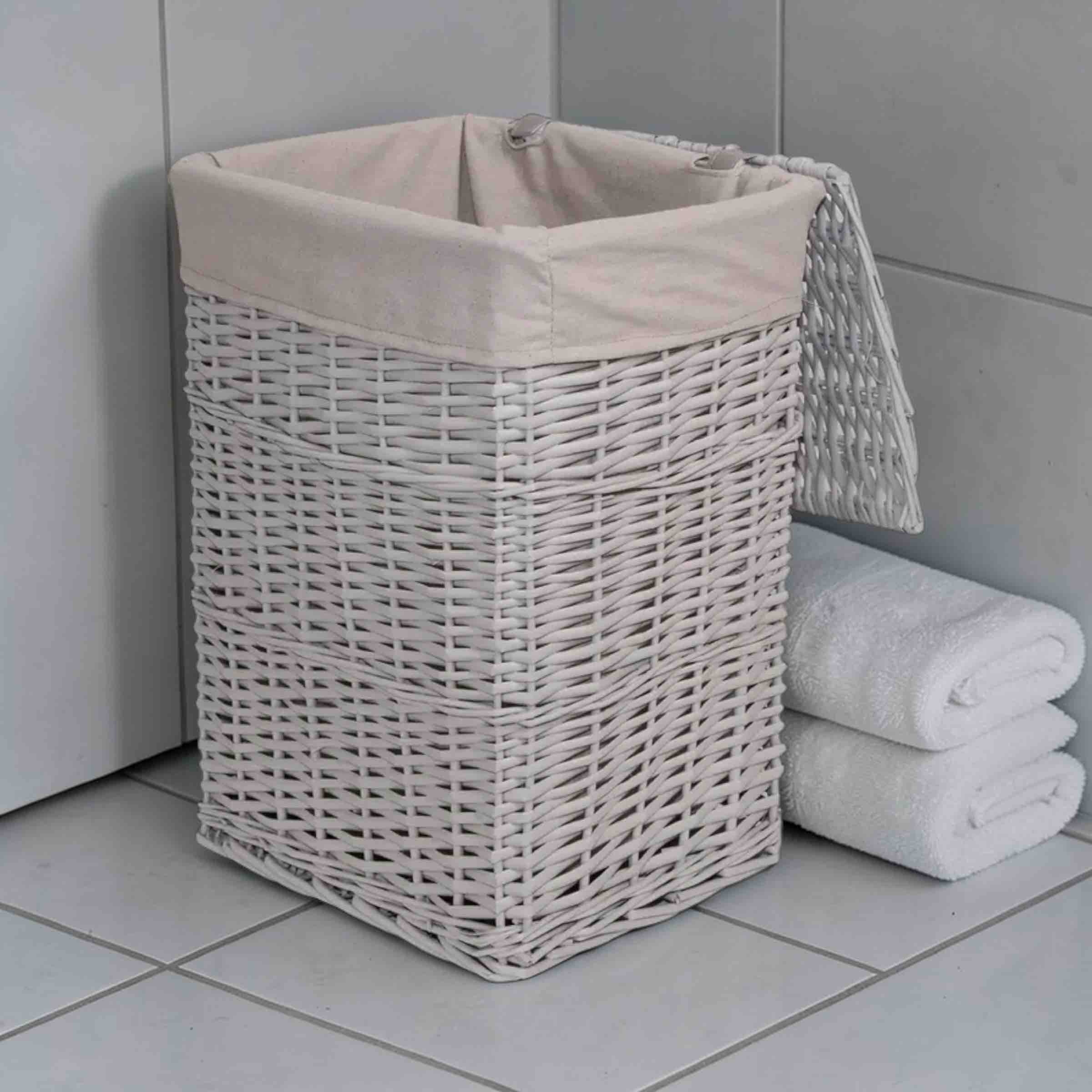 Wicker laundry basket with a beige liner next to folded towels on a tiled floor.