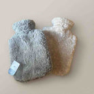 Two textured fleece hot water bottles, one in gray with a paper tag and one in beige, on a solid light beige background.