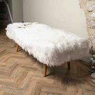 White fluffy bench on a wooden floor next to a fireplace.
