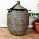 Woven basket with a lid on a wooden floor next to a plant