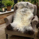 Fluffy sheepskin rug on a chair in a cozy room with plants and candles.