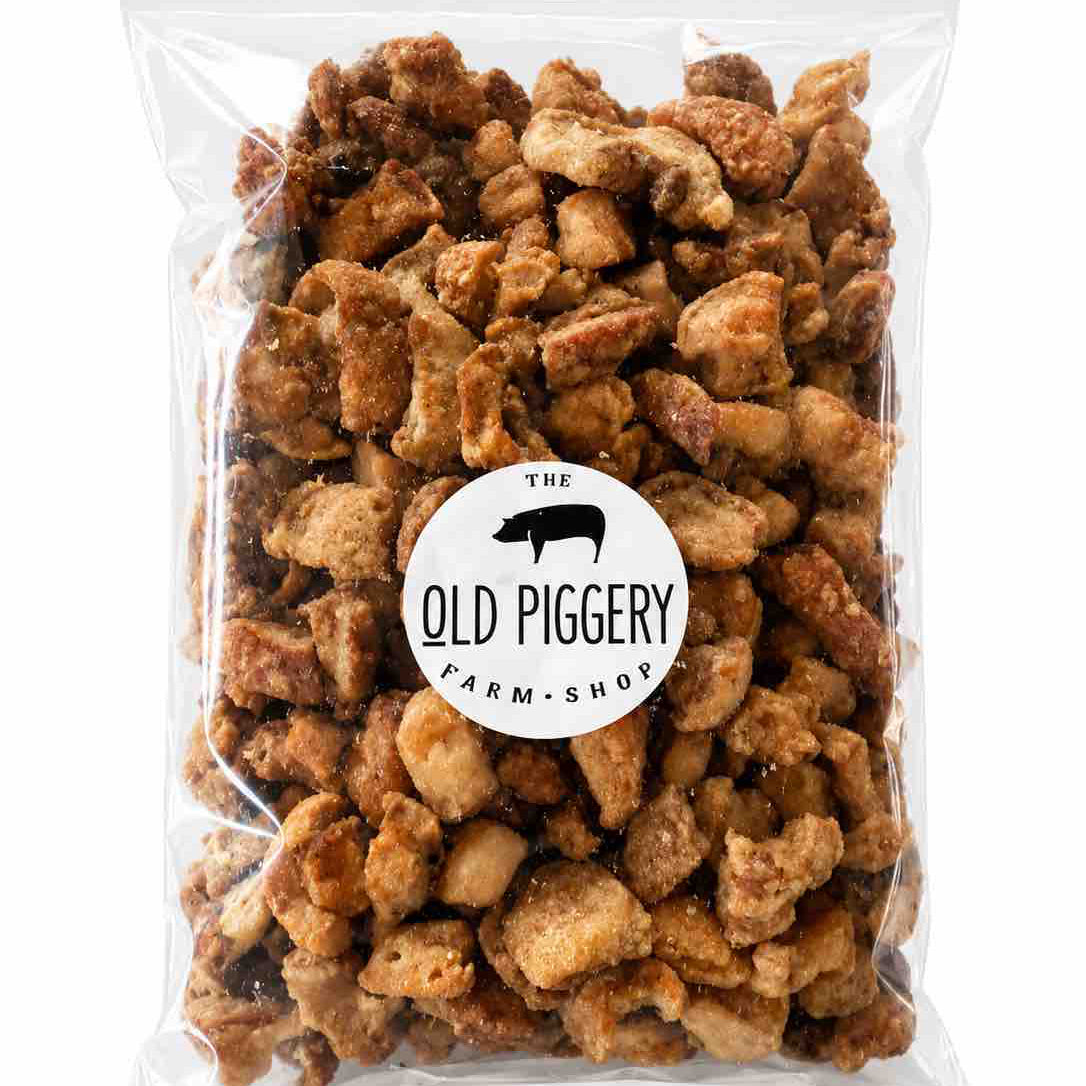 A clear plastic resealable bag filled with small browned snack pieces, featuring a round white label that reads 'The Old Piggery Farm Shop' with a black pig silhouette, on a white background.