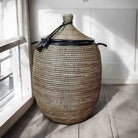 Woven storage basket with a lid on a wooden floor near a window.