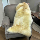 Beige fur throw draped over a gray armchair in a room with a wooden floor and a small table.