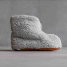 A single plush shearling slipper boot in light gray with a brown sole, photographed against a neutral gray background.