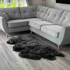 A light gray upholstered sectional sofa with tufted back cushions and tapered wooden legs, shown in a living room setting on a gray wood floor with a dark gray shag rug in front.