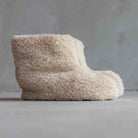 A single plush, ankle-height slipper in a warm cream or off-white sherpa/fleece material, photographed against a soft gray studio background.