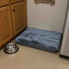 Pet bed with a fluffy cover next to a metal bowl on a carpeted floor.