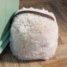 Fluffy white pillow with a brown leather strap on a wooden floor