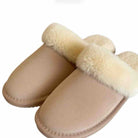 A pair of slip-on mule slippers with a beige suede-like upper and thick cream faux-fur trim around the opening, shown on a plain white background.