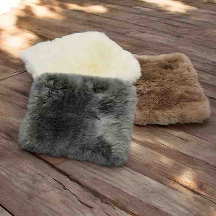 Three fur pillows in white, gray, and brown on a wooden deck.