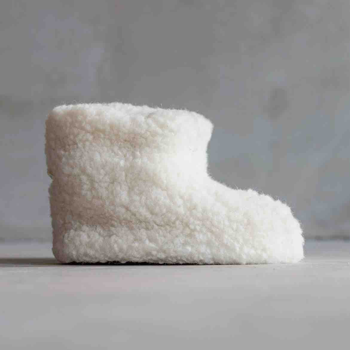 A single off-white sheepskin slipper boot shown in profile against a neutral gray background.