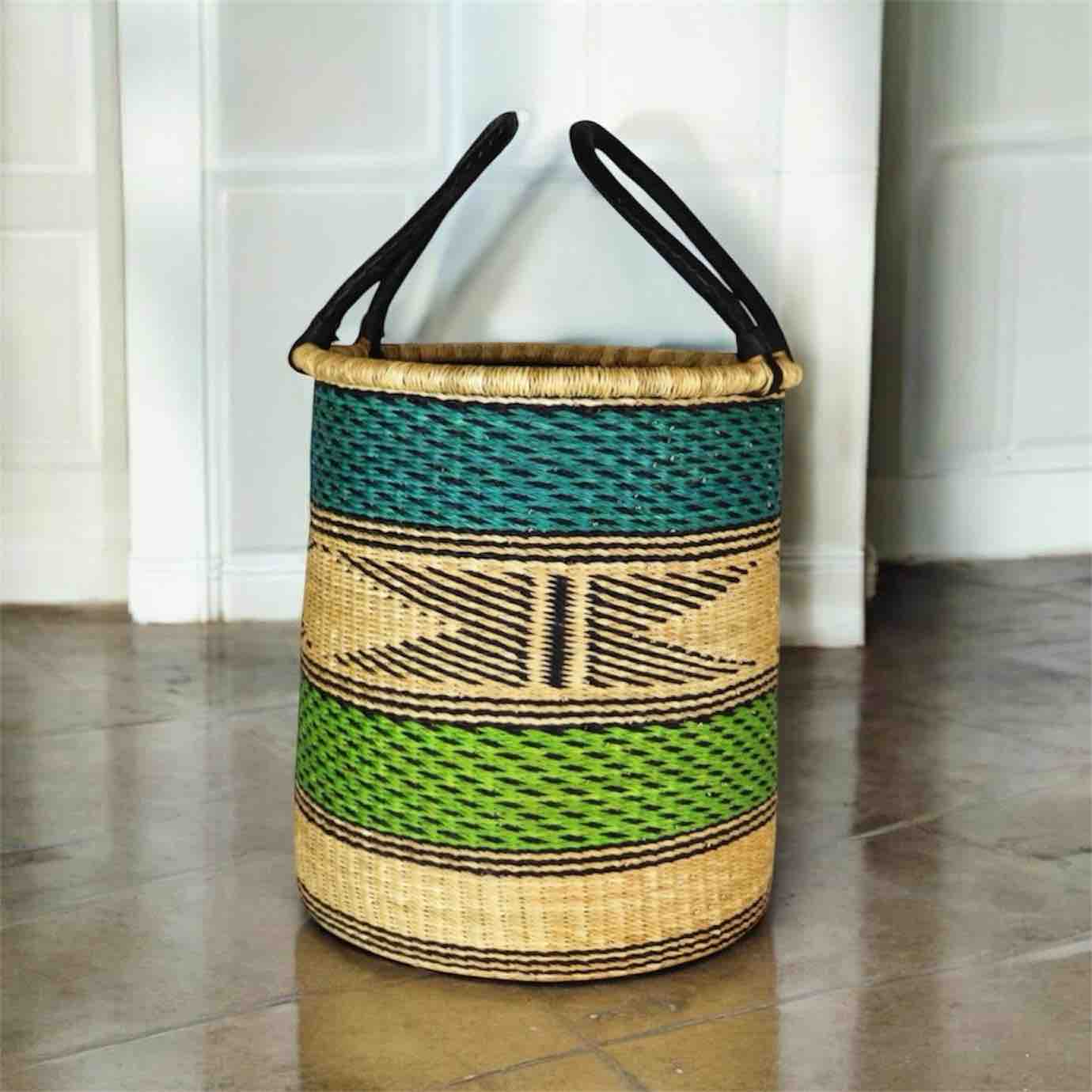 Woven laundry basket with black handles on a tiled floor