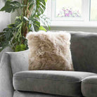 Gray sofa with a fluffy beige pillow in a room with plants and a window.