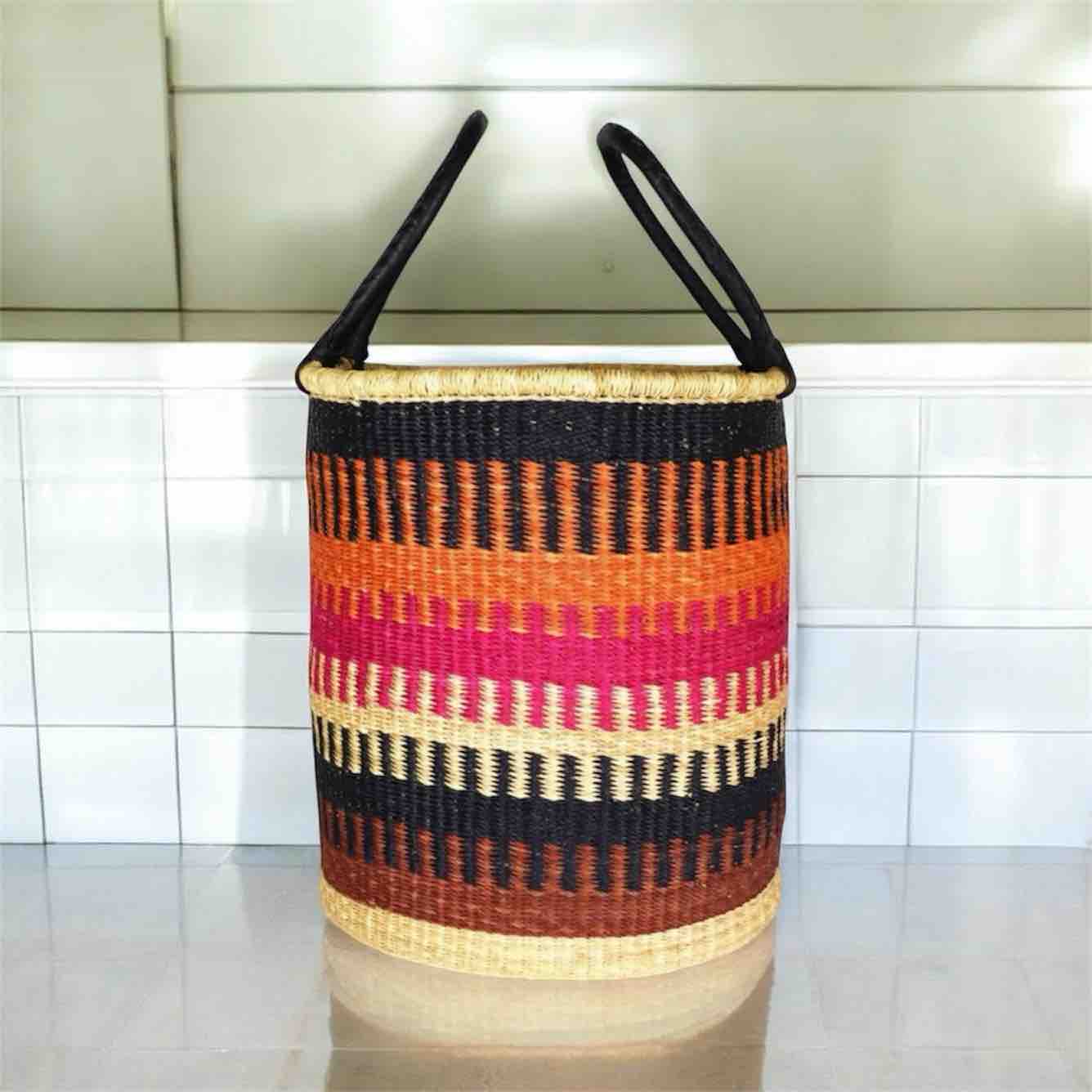 Colorful woven basket with black handles on a tiled floor