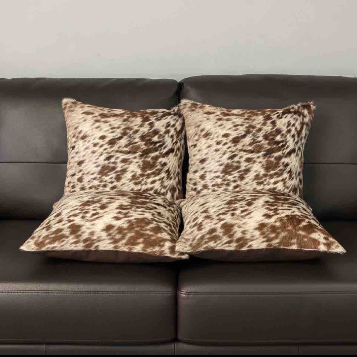 Two cowhide patterned pillows on a brown leather sofa.