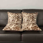 Two cowhide patterned pillows on a brown leather sofa.
