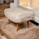 Fluffy ottoman with wooden legs on a brown rug in a living room setting.